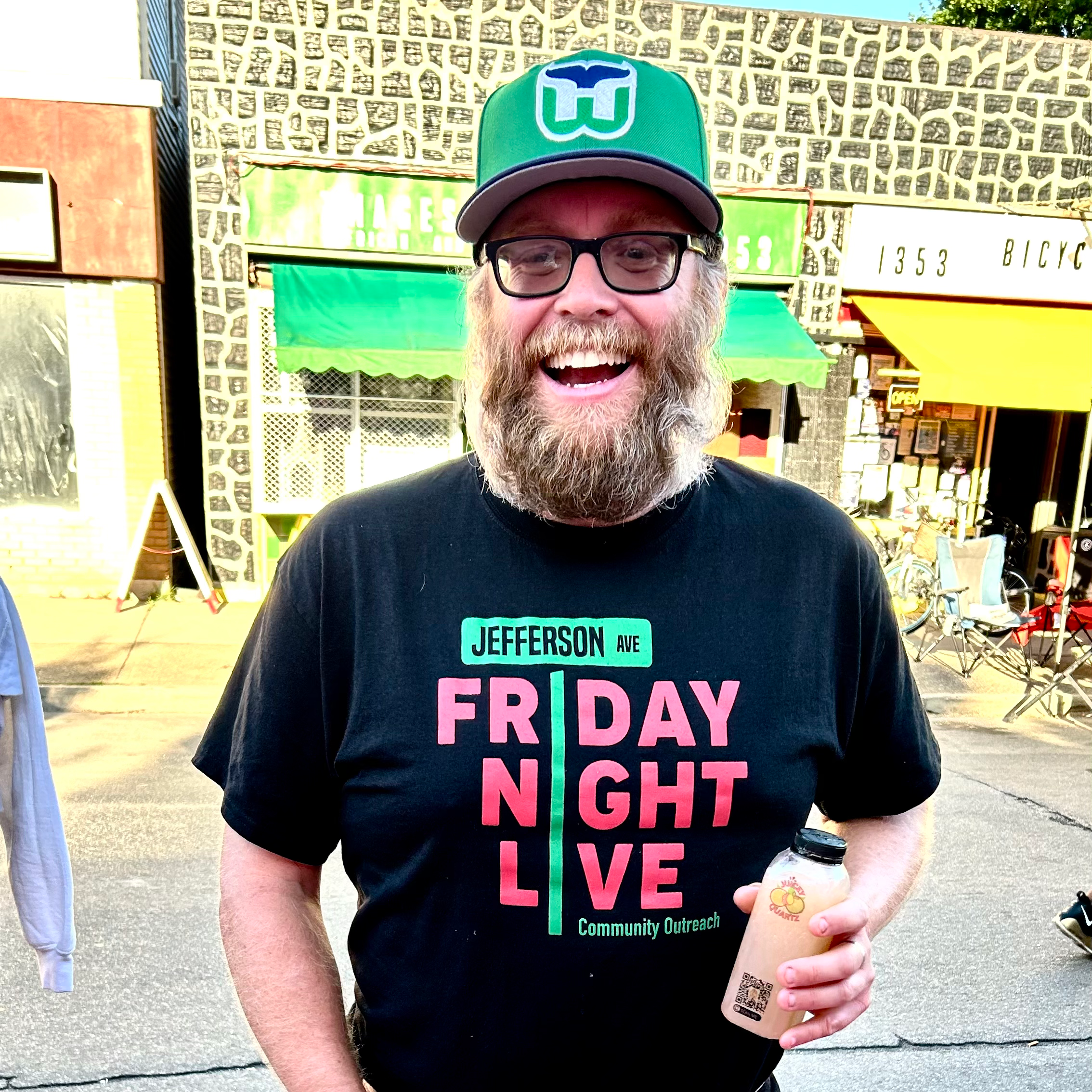 Man wearing a black t-shirt with colorful text, standing outdoors with drinks and straws on a table.